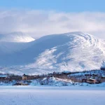 Beautiful scenery of buildings at foot of snowy mountains on coast of Lake Torneträsk (Tornestrask) around Abisko National Park (Abisko nationalpark). Sweden, Arctic Circle, Swedish Lapland